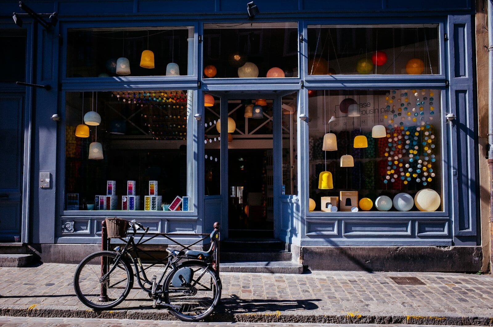 A bicycle parked on a cobblestone sidewalk in front of a lamp shop